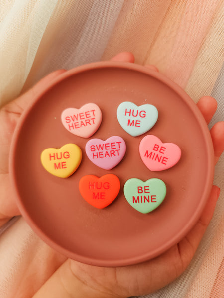 Heart-shaped candy conversation pieces on a terracotta plate held by a hand.